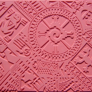 May include: Pink rubber stamp with a detailed design featuring geometric shapes, a stylized sun, and two lizards. The design is reminiscent of Aztec or Mayan art.
