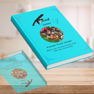Könnte beinhalten: Zwei türkisfarbene Kochbücher auf einer Holzoberfläche. Das Cover des oberen Buches zeigt den Text "Food Hunter" und "Korean Food recipe" mit einem Foto von koreanischen Gerichten. Der Text lautet "Machen Sie Ihr Lieblings-Koreanisches Essen mit Ihren eigenen Händen."