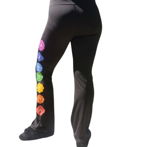 Puede incluir: Pantalones de yoga negros con un dise&ntilde;o de arco&iacute;ris de siete chakras en la pierna izquierda. Los chakras est&aacute;n representados por s&iacute;mbolos y colores.