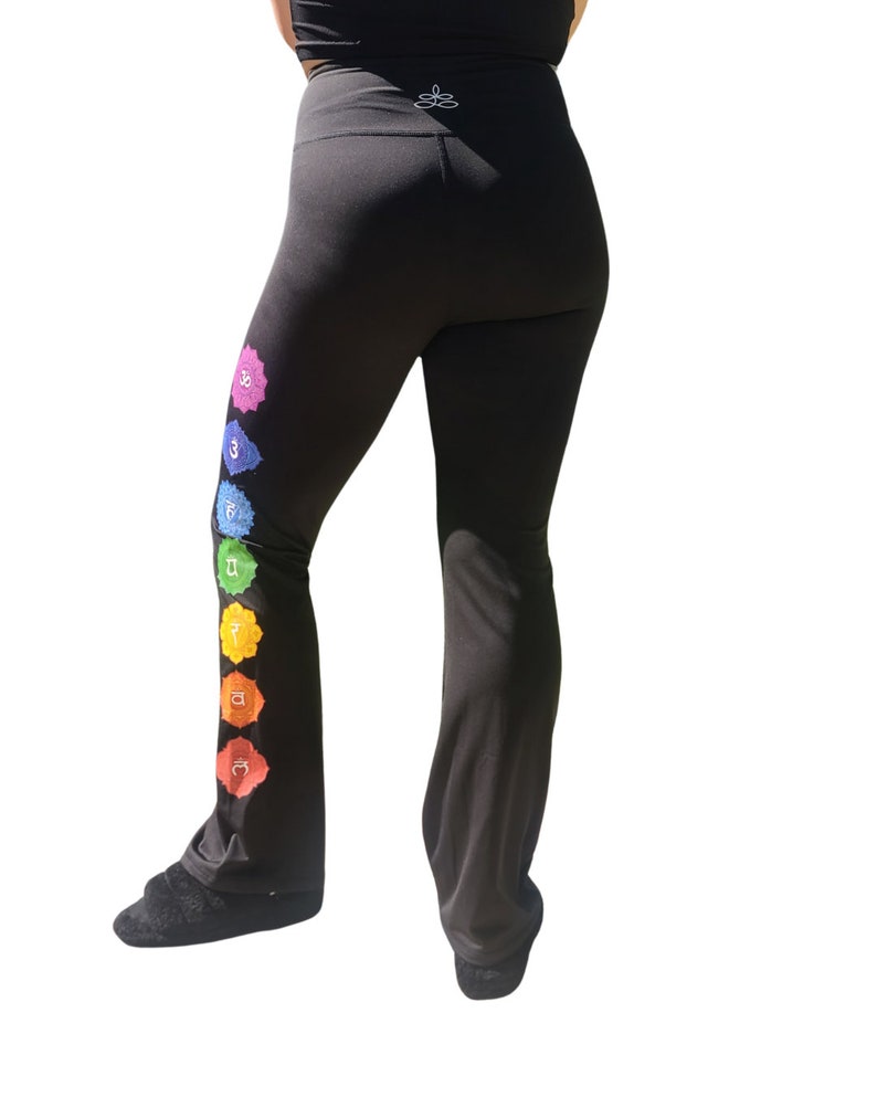 Puede incluir: Pantalones de yoga negros con un dise&ntilde;o de arco&iacute;ris de siete chakras en la pierna izquierda. Los chakras est&aacute;n representados por s&iacute;mbolos y colores.