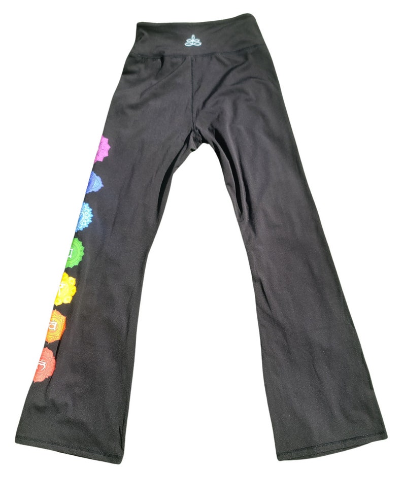 Puede incluir: Pantalones de yoga negros con un dise&ntilde;o de chakra colorido en la pierna izquierda. Los pantalones tienen cintura alta y pierna ancha.