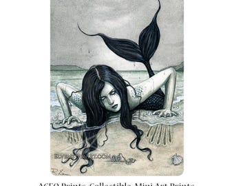 May include: A black and white illustration of a mermaid with long black hair, lying on her stomach on a sandy beach. Her tail is curled behind her and her head is resting on her arm. The mermaid has a sad expression on her face. The image is 2.5 inches by 3.5 inches.