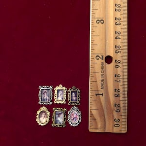 Könnte beinhalten: Miniatur-Porträts mit verzierten Rahmen in Gold, Silber und Bronze. Die Porträts zeigen Figuren in Vintage-Kleidung. Ein Holzlineal zeigt die Größe der Rahmen in Zentimetern.