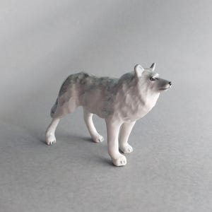 May include: A ceramic wolf figurine in a standing pose. The wolf has a gray and white coat, with detailed fur texture. The figurine is a decorative item, likely for display.