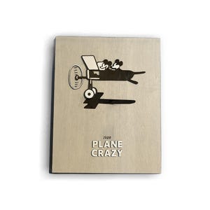 May include: A beige wooden plaque with a black silhouette of Mickey Mouse and a friend flying a plane. The text "1928 PLANE CRAZY" is printed below the image.