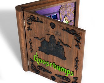 Puede incluir: Caja de madera con forma de libro de Goosebumps con una puerta con bisagras. La puerta presenta una silueta negra de una casa embrujada, murciélagos y la palabra "Goosebumps" en verde. El interior revela una escena en miniatura con una figura sosteniendo una poción.