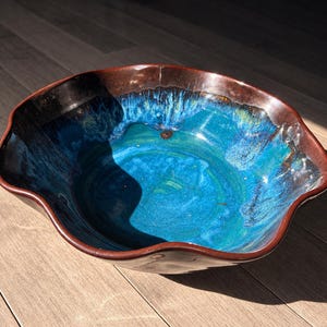 May include: A ceramic bowl with a wavy, scalloped rim featuring a deep brown exterior and a vibrant, multi-tonal interior glaze that transitions from dark navy blue at the edges to a bright, luminous turquoise blue in the centre basin.