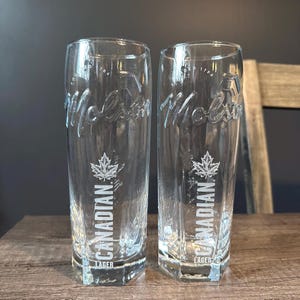 Peut inclure: Deux verres à bière transparents avec une base hexagonale. Chaque verre présente le texte en relief Molson, l'inscription ESTABLISHED 1786, un motif de feuille d'érable blanche et le texte imprimé blanc CANADIAN LAGER sur la face avant.