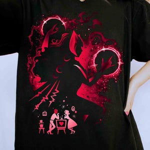 May include: Black t-shirt with a red graphic design. The design features a woman's silhouette with a halo, holding glowing orbs, and a couple at a table. The design has a cosmic theme.