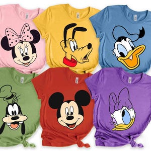 以下が含まれることがあります： ディズニーの漫画のキャラクターが描かれた、カラフルなTシャツのコレクション。ピンク、黄色、青、緑、赤、紫など、さまざまな色があります。各シャツには、ミニーマウス、プルート、ドナルドダック、グーフィー、ミッキーマウス、デイジーダックなど、さまざまなキャラクターが表示されています。