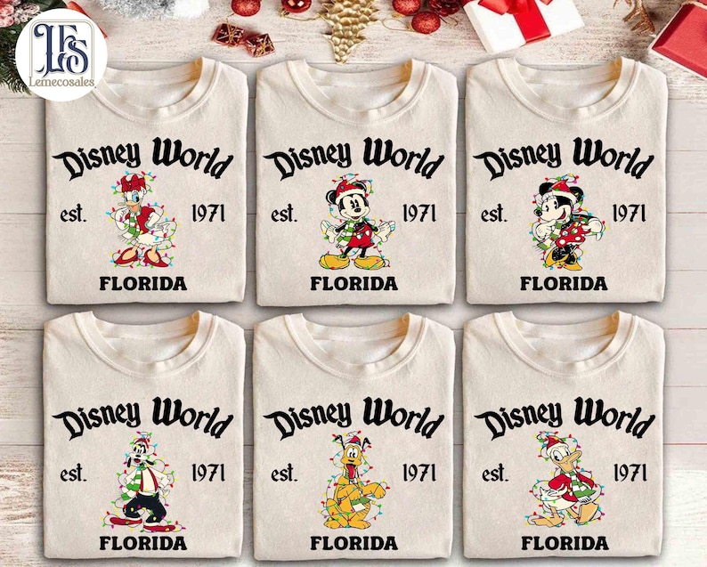 May include: Six cream-colored t-shirts with the words "Disney World" and "Florida" printed in black. Each shirt features a different Disney character decorated with Christmas lights. The shirts are from 1971.