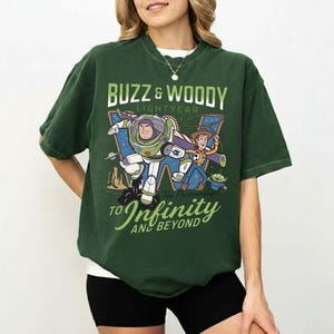 May include: Dark green t-shirt featuring Buzz Lightyear and Woody from Toy Story. The graphic includes the text "Buzz & Woody Lightyear" and "To Infinity and Beyond". The shirt is a relaxed fit.