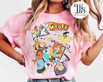 May include: Pink t-shirt featuring a colorful graphic from "A Goofy Movie." The design includes cartoon characters Goofy, Max, and others, with the movie title in bold letters. The background has a grid pattern with abstract shapes.