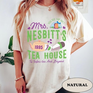 Peut inclure: Un t-shirt blanc avec un motif graphique vert, violet et rose qui dit "Mrs. Nesbitt's Tea House 1995 To Infini-tea And Beyond". Le graphique comprend une th&eacute;i&egrave;re, une fus&eacute;e et des c&oelig;urs.