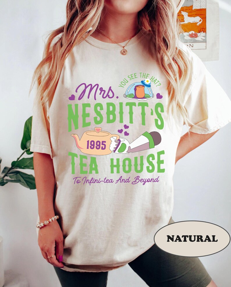 Peut inclure: Un t-shirt blanc avec un motif graphique vert, violet et rose qui dit "Mrs. Nesbitt's Tea House 1995 To Infini-tea And Beyond". Le graphique comprend une th&eacute;i&egrave;re, une fus&eacute;e et des c&oelig;urs.
