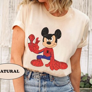 May include: A cream colored t-shirt with a cartoon image of Mickey Mouse dressed as Spiderman. The text "NATURAL" is visible in the lower left corner of the image.