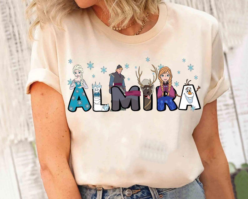 Puede incluir: Una camiseta blanca con un gr&aacute;fico de los personajes de la pel&iacute;cula Frozen. El gr&aacute;fico incluye a Elsa, Anna, Olaf, Kristoff y Sven. Los personajes est&aacute;n dispuestos para deletrear el nombre "ALMIRA".