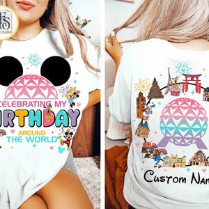 Op de afbeelding: Wit T-shirt met een kleurrijk grafisch ontwerp. De voorkant heeft een Mickey Mouse-hoofd met de tekst "Celebrating My Birthday Around The World". De achterkant heeft een globe-ontwerp omringd door bezienswaardigheden en de tekst "Custom Name."