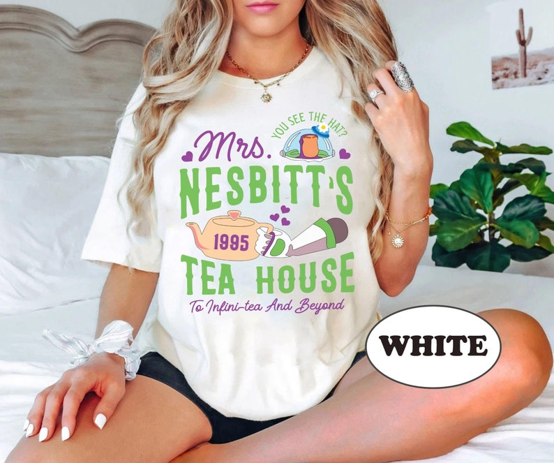 Peut inclure: T-shirt blanc avec un motif graphique violet et vert qui dit "Mrs. Nesbitt's Tea House 1995 To Infini-tea And Beyond" et repr&eacute;sente une th&eacute;i&egrave;re et une tasse &agrave; th&eacute; de dessin anim&eacute;.
