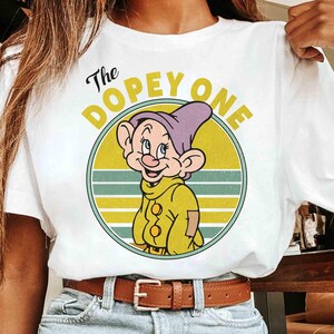 May include: White t-shirt featuring a cartoon image of Dopey from Snow White. The graphic includes Dopey's face inside a yellow circle with the text "The Dopey One". The design has a vintage, retro style.