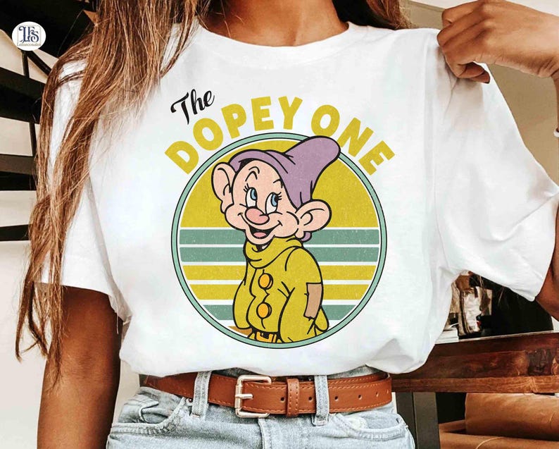 May include: White t-shirt featuring a cartoon image of Dopey from Snow White. The graphic includes Dopey's face inside a yellow circle with the text "The Dopey One". The design has a vintage, retro style.