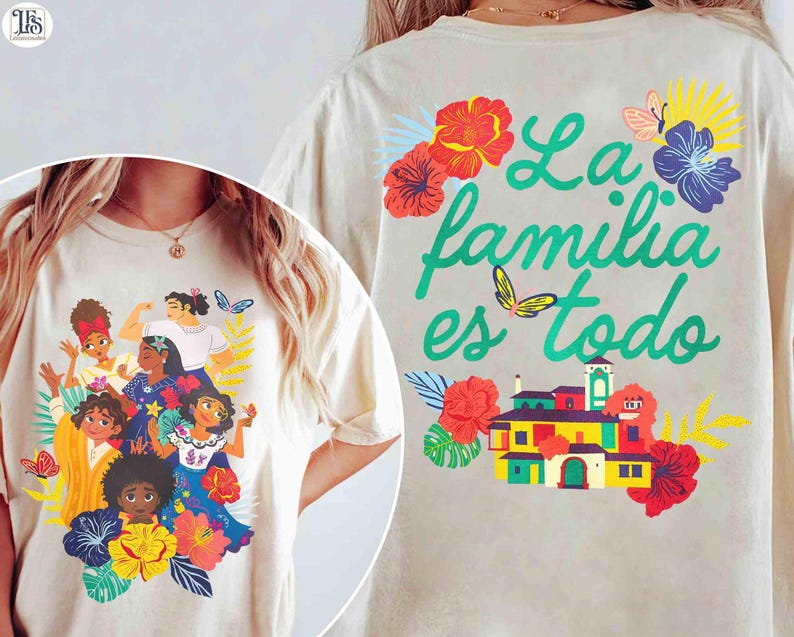 May include: Cream-colored t-shirt featuring a colorful illustration of several women surrounded by flowers and butterflies. The back of the shirt displays the text "La familia es todo" in green, along with a vibrant house graphic and floral accents.
