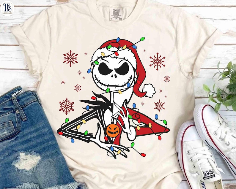Puede incluir: Camiseta color crema con un dise&ntilde;o de Jack Skellington con gorro de Pap&aacute; Noel, adornado con luces navide&ntilde;as y una calabaza. Copos de nieve rojos dispersos alrededor del dise&ntilde;o. La camiseta se combina con pantalones cortos de mezclilla y zapatillas blancas.