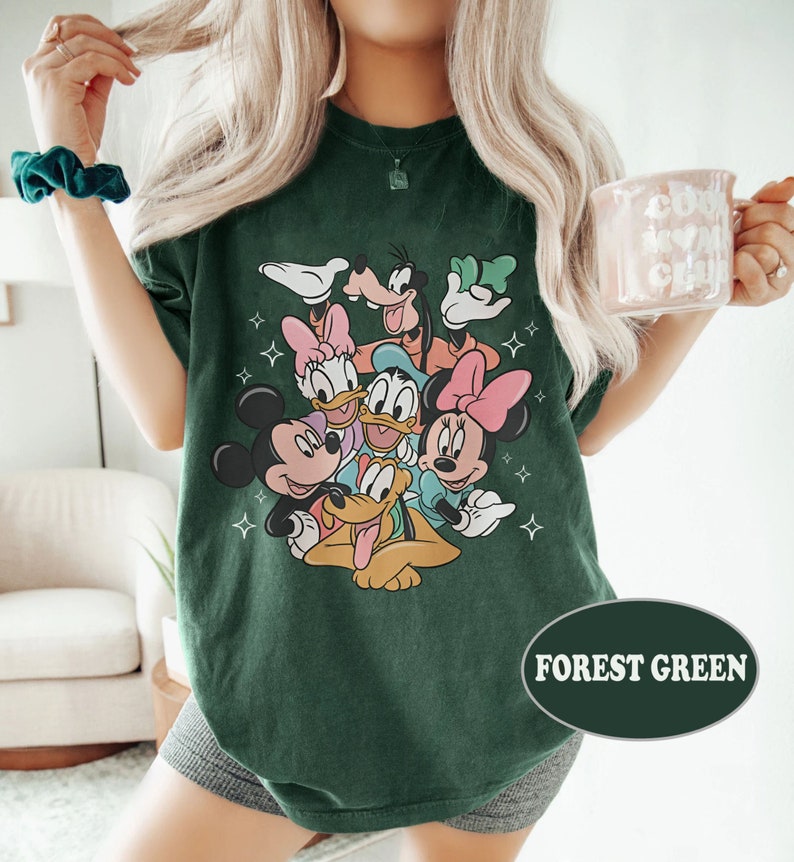 May include: A forest green t-shirt with a graphic print of Mickey Mouse, Minnie Mouse, Donald Duck, Goofy, and Pluto. The characters are arranged in a circle with their heads facing the center. The shirt has a relaxed fit and a crew neck.