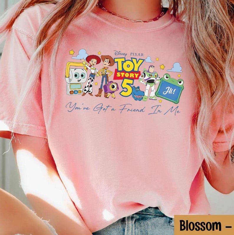 May include: Pink t-shirt featuring a graphic of characters from the Disney Pixar movie Toy Story 5. The design includes Woody, Buzz Lightyear, and other characters, with the text "You've Got a Friend In Me".