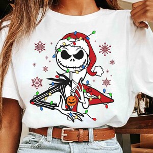 Puede incluir: Camiseta blanca con un dise&ntilde;o de Jack Skellington de The Nightmare Before Christmas, con un gorro de Pap&aacute; Noel y luces navide&ntilde;as. El dise&ntilde;o incluye copos de nieve y una calabaza. Un art&iacute;culo festivo de vacaciones.