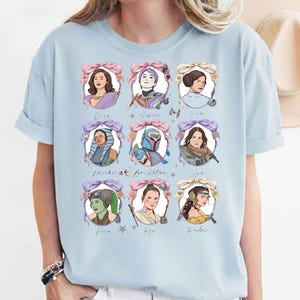 May include: Pale blue t-shirt with nine portraits of female characters from a science fiction franchise, each within a decorative bow. The portraits are in a vintage style, with names below. The shirt is made of a soft material, suitable for casual wear.