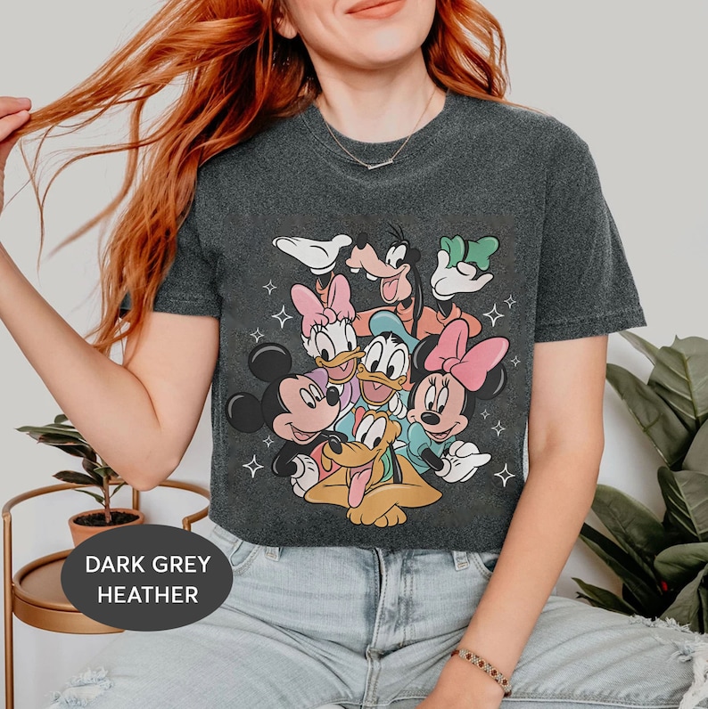 May include: Dark grey heather cropped t-shirt featuring a graphic print of Mickey Mouse, Minnie Mouse, Donald Duck, Goofy, Pluto, and Daisy Duck. The characters are arranged in a playful, overlapping design.