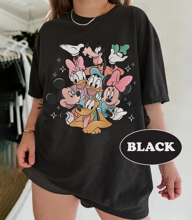 May include: Black t-shirt with a graphic print of Mickey Mouse, Minnie Mouse, Donald Duck, Goofy, and Pluto. The characters are all smiling and appear to be hugging each other. The shirt has a distressed look and is made of a soft, comfortable fabric.