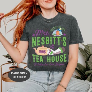 Peut inclure: T-shirt en jersey chin&eacute; gris fonc&eacute; avec un motif vert, violet et jaune repr&eacute;sentant une th&eacute;i&egrave;re, un personnage et le texte "You see the hat? Mrs. Nesbitt's 1995 Tea House To Infini-tea And Beyond".