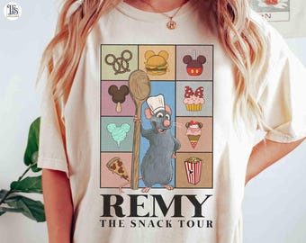 Può includere: T-shirt beige con un'illustrazione a cartoni animati di Remy il ratto che tiene un cucchiaio di legno, circondato da icone di cibo in una griglia. Il testo "REMY THE SNACK TOUR" è stampato sotto.