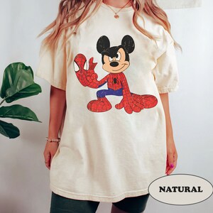 May include: A cream colored t-shirt with a vintage cartoon image of Mickey Mouse dressed as Spiderman. The text "NATURAL" is visible in the bottom right corner of the image.