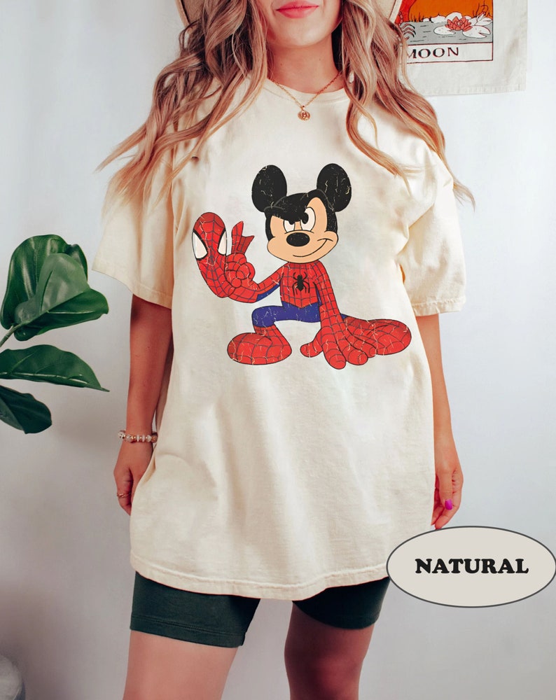 May include: A cream colored t-shirt with a vintage cartoon image of Mickey Mouse dressed as Spiderman. The text "NATURAL" is visible in the bottom right corner of the image.