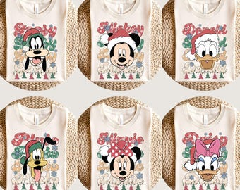 May include: Six white t-shirts with different Christmas-themed Disney characters. The characters are Pluto, Mickey Mouse, Minnie Mouse, Donald Duck, and Daisy Duck. Each shirt has the character's name in a festive font and a Christmas tree design.