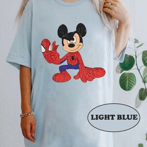 May include: Light blue t-shirt featuring a cartoon image of Mickey Mouse dressed as Spider-Man. The image has a vintage, distressed look.