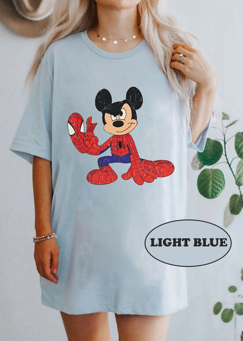 May include: Light blue t-shirt featuring a cartoon image of Mickey Mouse dressed as Spider-Man. The image has a vintage, distressed look.