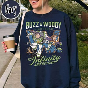 May include: Navy blue sweatshirt featuring Buzz Lightyear and Woody from Toy Story. The graphic includes the text "BUZZ & WOODY LIGHTYEAR" and "TO INFINITY AND BEYOND". The design is in shades of green, white, blue, and brown.