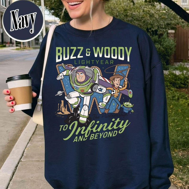 May include: Navy blue sweatshirt featuring Buzz Lightyear and Woody from Toy Story. The graphic includes the text "BUZZ & WOODY LIGHTYEAR" and "TO INFINITY AND BEYOND". The design is in shades of green, white, blue, and brown.