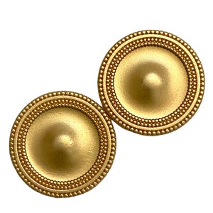 May include: A pair of gold-toned metal earrings with a circular design. The earrings have a raised, domed centre and a beaded border.