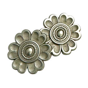 Puede incluir: Dos botones de metal plateado en forma de flor con un círculo central elevado y un diseño texturizado.