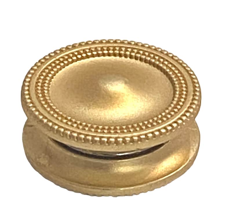 May include: A gold-toned metal button with a decorative beaded edge. The button has a domed top and a flat bottom.