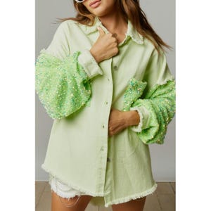 May include: A light green denim shirt with sequined sleeves. The shirt has a button-down front and a relaxed fit.