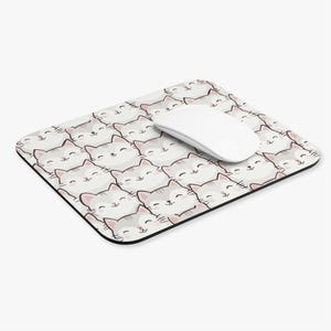 Puede incluir: Una alfombrilla de ratón rectangular con un patrón repetido de caras de gatos de dibujos animados sonrientes en gris y blanco. Un ratón inalámbrico blanco descansa sobre la alfombrilla. La alfombrilla tiene un borde negro.