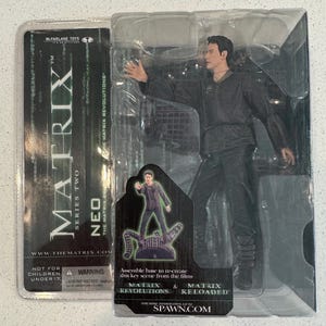 May include: A McFarlane Toys action figure of Neo from The Matrix: Revolutions. The figure is in a clear plastic package. The figure is wearing a black outfit and has his arm outstretched. The packaging includes the text "MATRIX SERIES TWO NEO THE MATRIX REVOLUTIONS".