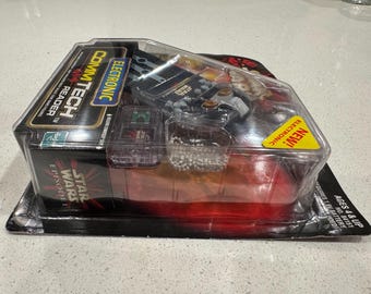 Könnte beinhalten: Ein Star Wars Episode I CommTech Reader Spielzeug in seiner Originalverpackung. Die Verpackung ist schwarz mit roten und gelben Akzenten, und das Spielzeug ist durch ein transparentes Kunststofffenster sichtbar. Der Text "ELECTRONIC" und "NEW!" ist enthalten.