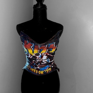Pode incluir: Um manequim preto vestindo uma camiseta azul e laranja com a palavra "KISS" e o texto "Alive in '75" impresso nela.